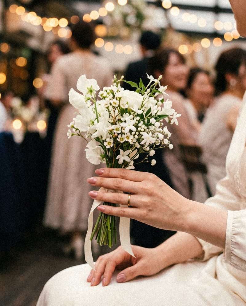 結婚式で花束を持つダスティピンクのネイルの手元（デモ用生成画像）
